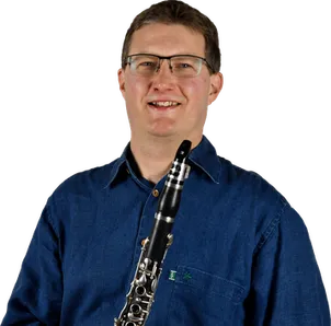 Ein Mann mit Brille und blauem Hemd lächelt und hält eine Klarinette in den Händen.