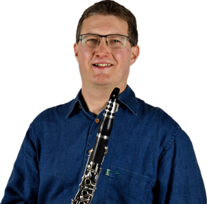 Ein Mann mit Brille und blauem Hemd lächelt und hält eine Klarinette in den Händen.