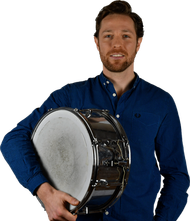 Ein Mann mit Bart hält eine Snare-Trommel in den Händen. Er trägt ein blaues Hemd.