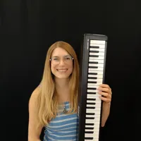 Eine Frau mit blonden Haaren lächelt und hält ein schwarz-weißes Keyboard.