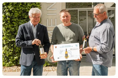 Drei Männer posieren mit Weinflaschen und einem Zertifikat, lächelnd. Der Mann in der Mitte hält ein Zertifikat mit dem Titel 'Weidener Gemeindewein'.
