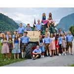 Eine Gruppe von Menschen in traditioneller deutscher Kleidung steht vor einem Traktor mit dem Wort 'Schonwies' darauf.