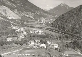 Eine Schwarz-Weiß-Luftaufnahme einer kleinen Stadt zwischen Bergen und einem mäandrierenden Fluss.