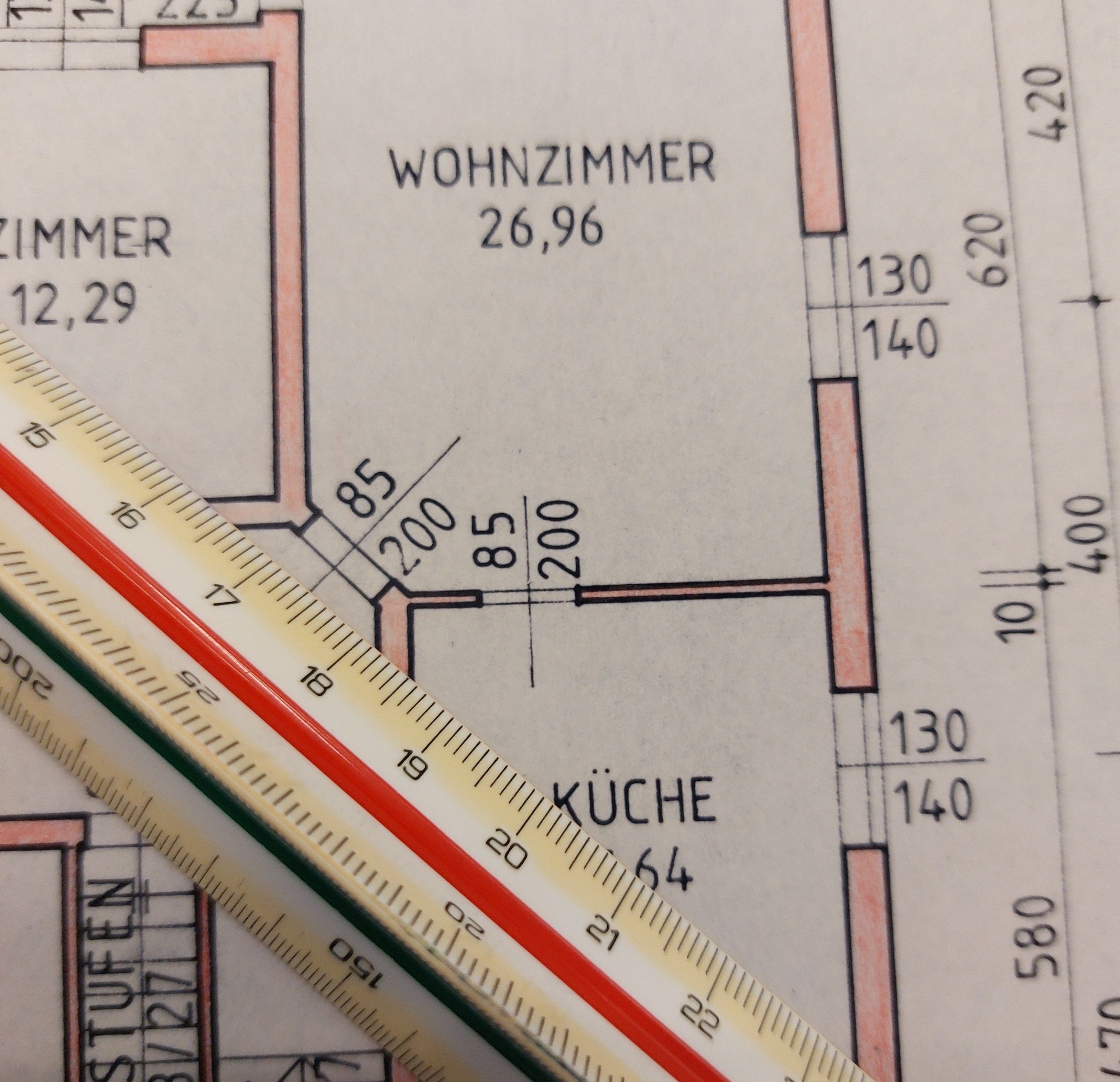 Ein Grundriss mit Abmessungen von Zimmern und einem Lineal. Das Wohnzimmer misst 26,96 m, während die Küche 12,29 m beträgt. Das Lineal ist in Zentimetern und Zoll markiert.