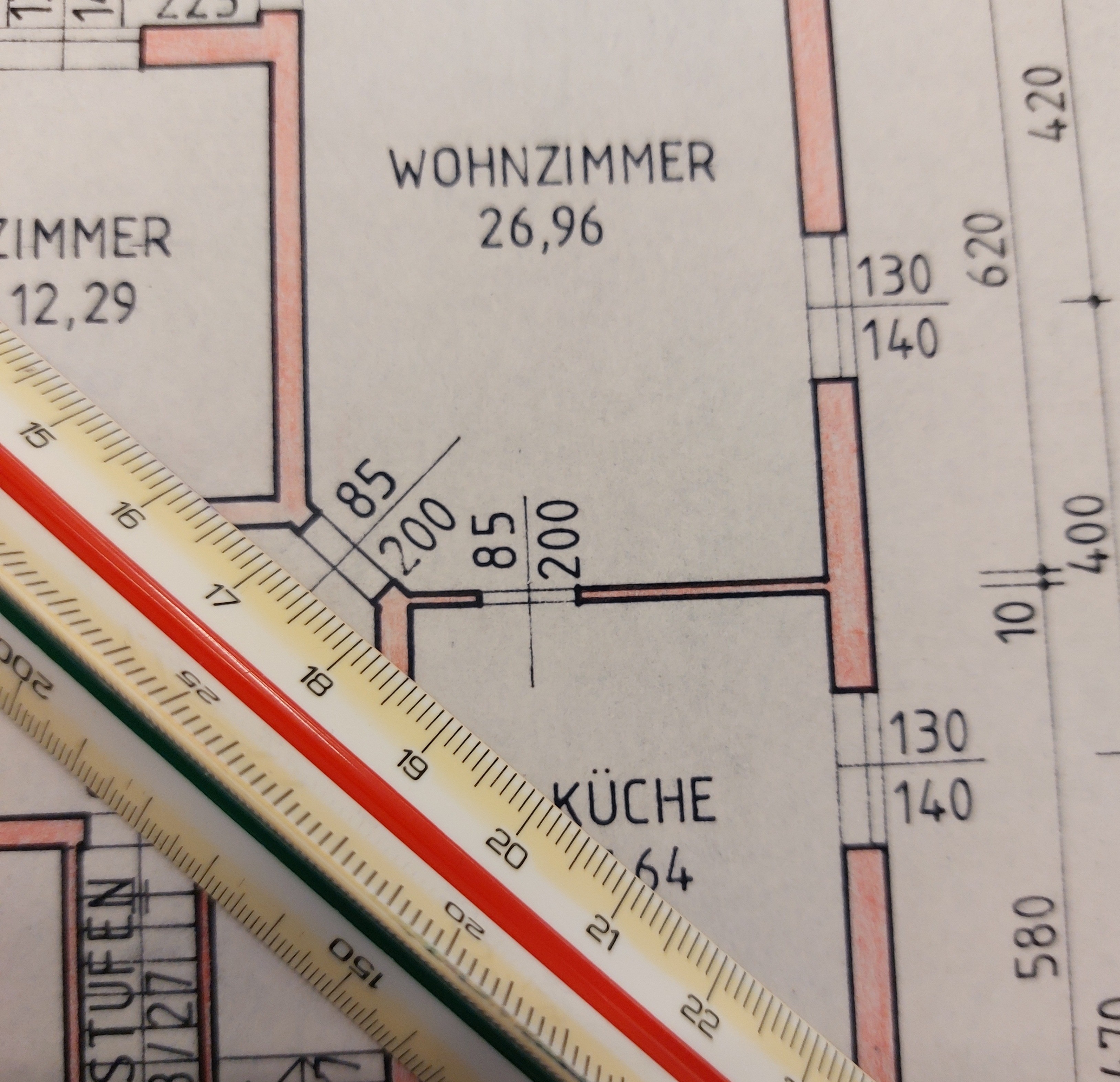 Ein Grundriss mit Abmessungen von Zimmern und einem Lineal. Das Wohnzimmer misst 26,96 m, während die Küche 12,29 m beträgt. Das Lineal ist in Zentimetern und Zoll markiert.