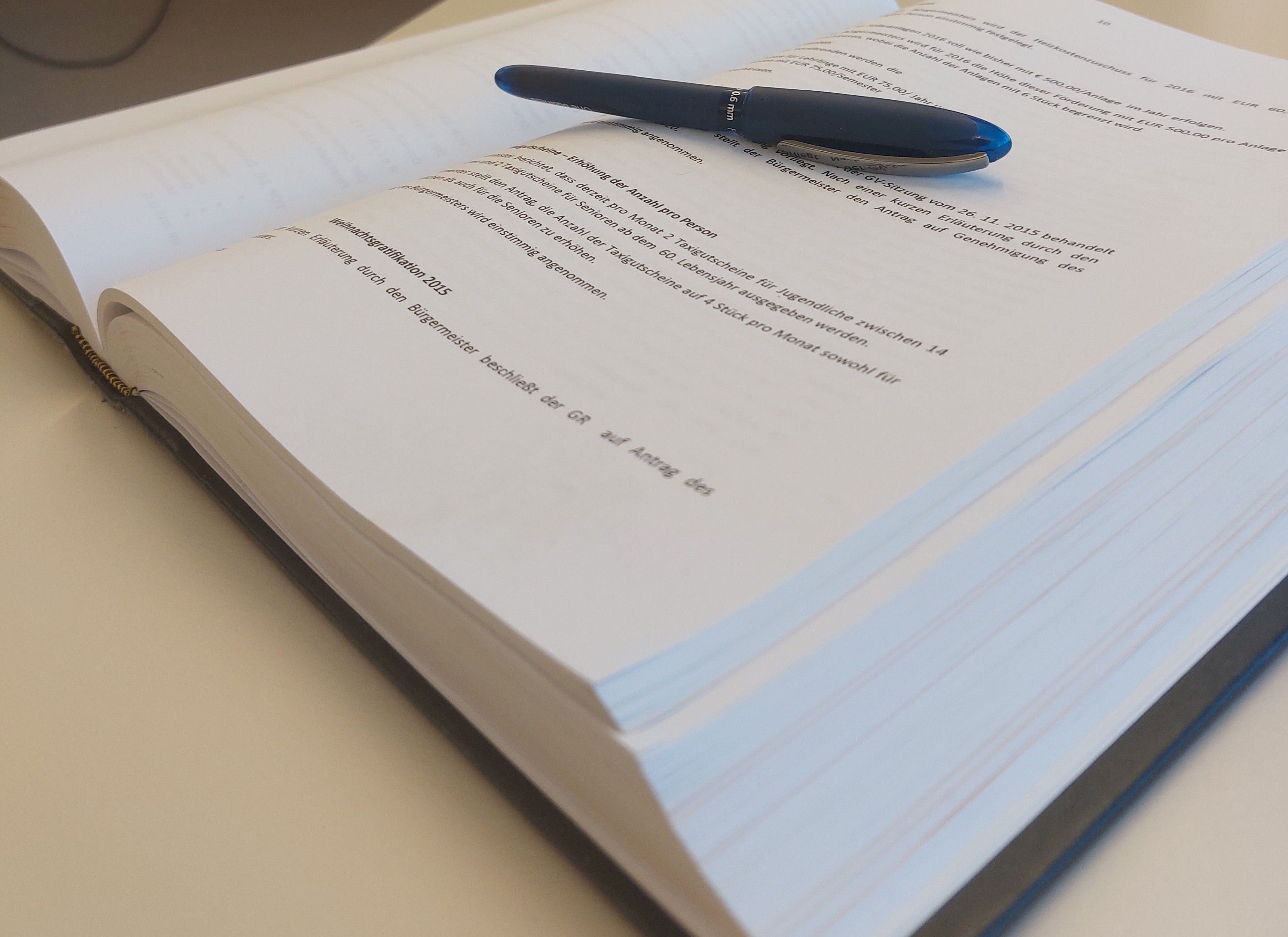 Ein offenes Buch mit mehreren Seiten, auf dem ein blauer Stift liegt. Der Text auf der Seite handelt von einer Lebensversicherungspolice.