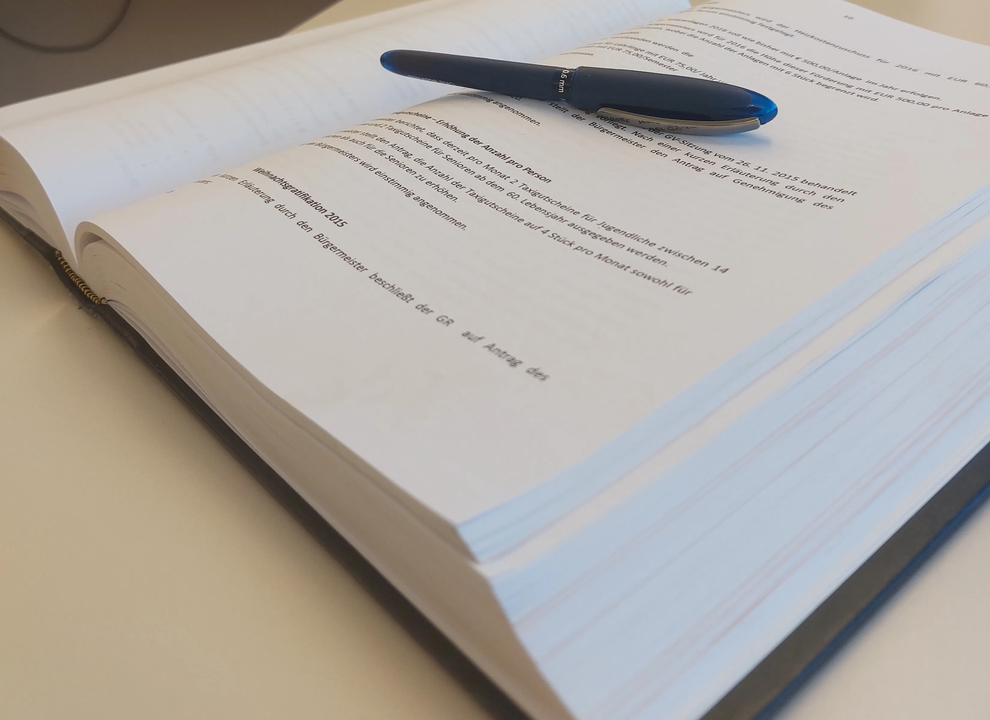 Ein offenes Buch mit mehreren Seiten, auf dem ein blauer Stift liegt. Der Text auf der Seite handelt von einer Lebensversicherungspolice.