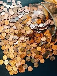 Eine Ansammlung von Kupfer-Cents, die aus einem Glasbecher auf eine schwarze Oberfläche verschüttet wurden. Einige Münzen sind glänzend, andere sind angeschliffen.
