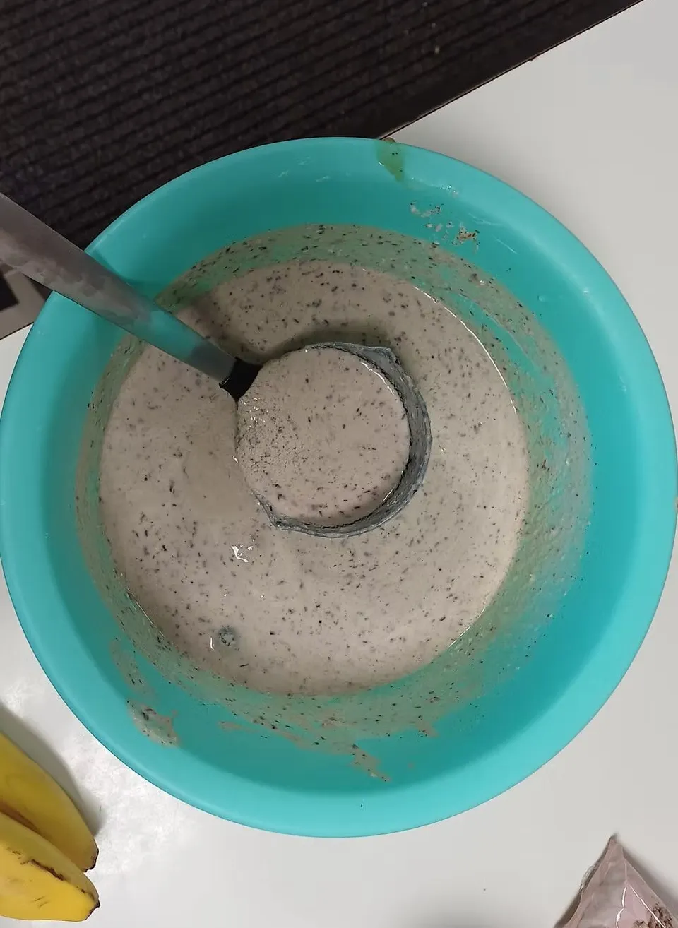 Ein türkisfarbener Behälter gefüllt mit einer cremigen Mischung, möglicherweise ein Dressing oder eine Sauce, mit einem Schöpflöffel, der etwas herausnimmt.