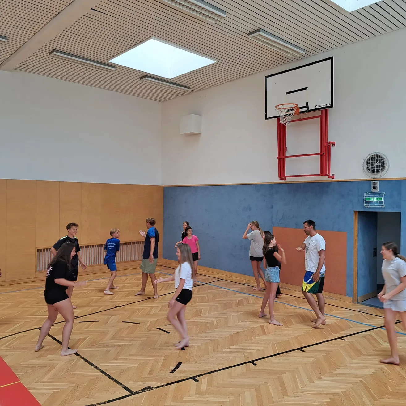 Eine Gruppe von Menschen spielt ein Spiel in einer Turnhalle mit einem Basketballkorb an der Wand.