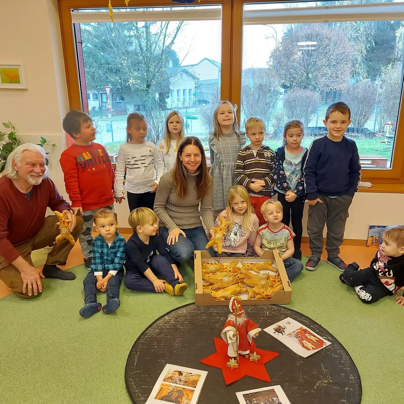 Eine Gruppe von Kindern und Erwachsenen versammelt sich um einen Tisch mit einer Schachtel Kekse und einer Weihnachtsmannfigur. Sie lächeln und posieren für ein Foto.
