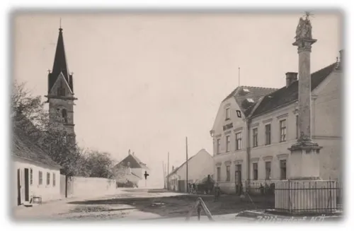 Ein altes Schwarz-Weiß-Foto einer Straße mit Gebäuden, einem Kirchturm und einem Denkmal.