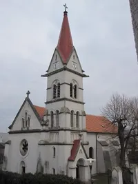 Eine alte Kirche mit einem roten Dach und einem Turm mit einer Uhr. Das Gebäude ist weiß und weist einige Abnutzungserscheinungen auf.