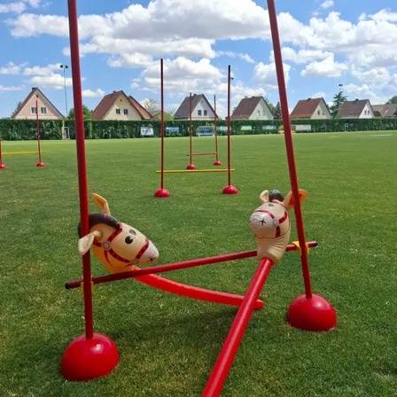 Zwei aufblasbare Spielzeugpferde sind an einer roten Hindernisparcours auf einem grünen Feld befestigt, mit Häusern im Hintergrund.