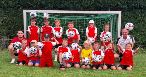 Eine Gruppe junger Fußballer in roten und weißen Trikots posiert für ein Foto mit Fußballbällen auf dem Kopf und in den Händen.