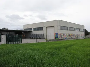 Ein großes weißes Industriegebäude mit einer Wandmalerei an der Seite, umgeben von einem Zaun und Gras.
