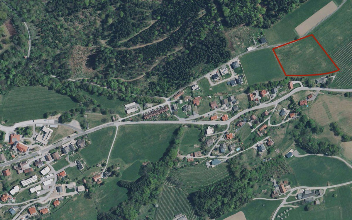 Eine Luftaufnahme eines kleinen Dorfes mit mehreren Häusern, Straßen und Feldern. Das Dorf ist von grünen Bäumen und Büschen umgeben. Es gibt ein großes offenes Feld, das in der oberen rechten Ecke mit einem roten Quadrat markiert ist.