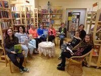 Eine Gruppe von Frauen sitzt in einem Buchladen in Stühlen und liest Bücher. Sie sind von Bücherregalen umgeben.