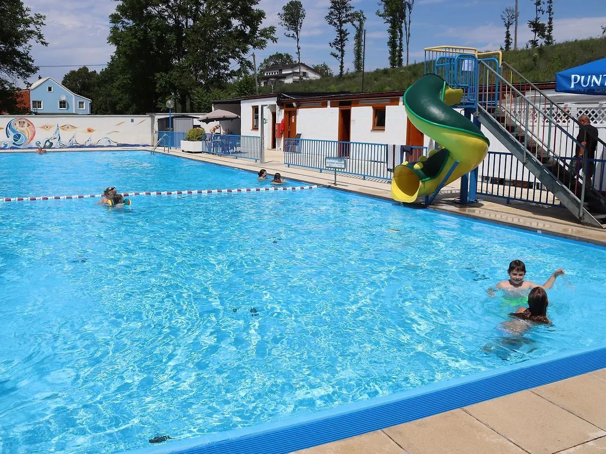 Kinder schwimmen in einem Schwimmbad in einem Park mit einem gelben und grünen Rutschvergnügen.