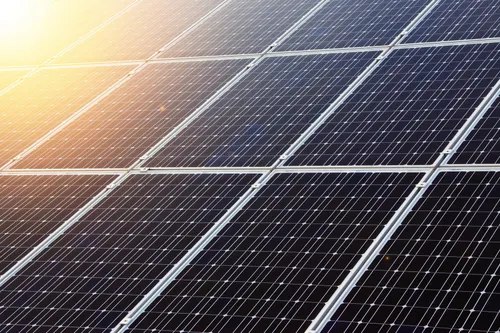 Nahaufnahme von Solarmodulen, die die Sonnenstrahlen reflektieren. Die Module sind in einem Rastermuster angeordnet.