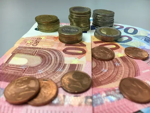 Ein Haufen Euro, bestehend aus Münzen und Banknoten, auf einer grauen Oberfläche. Die Münzen sind in verschiedenen Werten.
