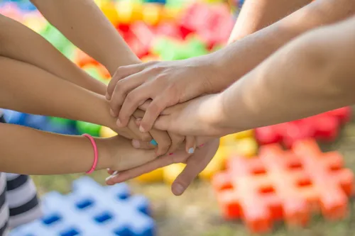 Eine Gruppe von Kindern hält sich im Kreis an den Händen, mit verschiedenen farbigen Spielzeugen im Hintergrund.