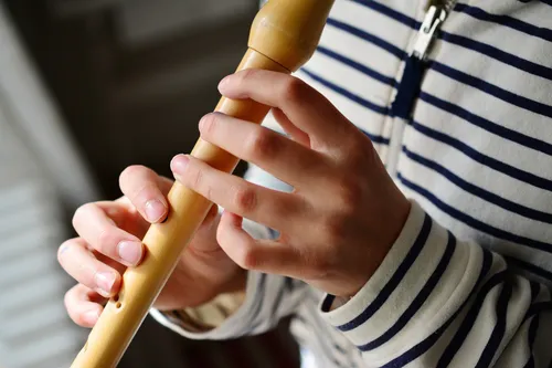 Eine Person spielt eine Holzflöte. Sie trägt ein gestreiftes Shirt und hat Finger an den Löchern der Flöte.