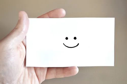Eine Hand hält eine weiße Karte mit einem gezeichneten Smiley-Gesicht darauf. Die Karte ist schlicht und weiß.