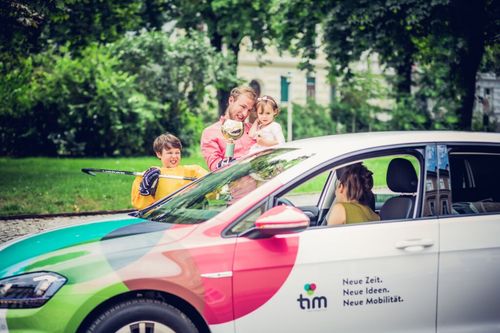Ein Mann hält eine Trophäe und ein Mädchen, während ein Junge einen Hockeyschläger hält. Sie stehen neben einem Auto mit den Worten Neue Zeit. Neue Ideen. Neue Mobilität. an der Seite.