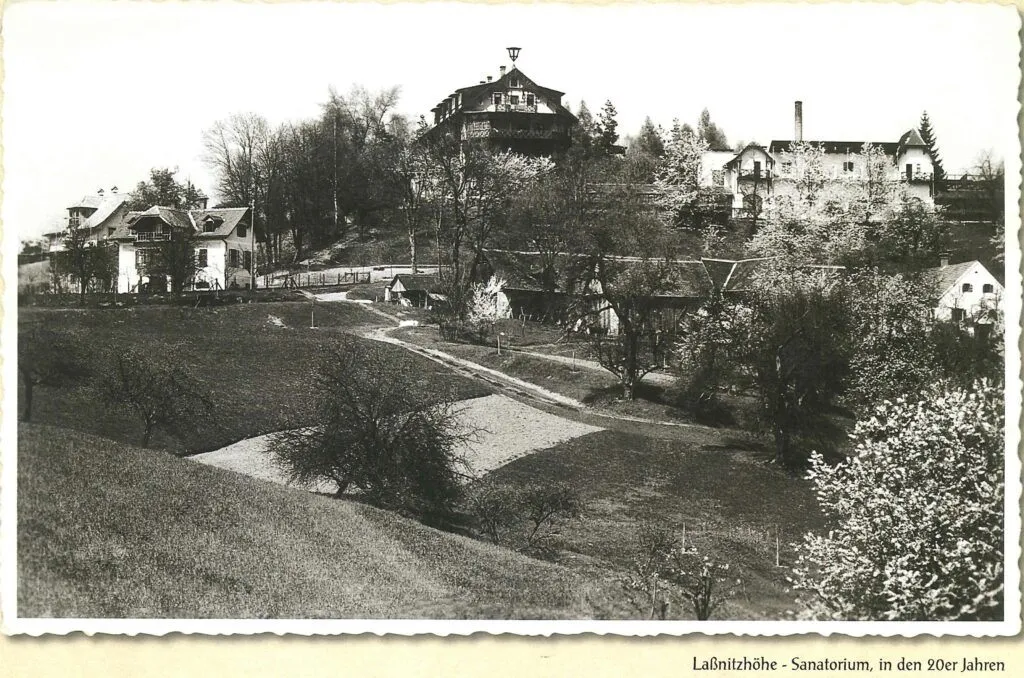Ein Schwarz-Weiß-Foto eines Hügels mit Häusern, Bäumen und einem großen Gebäude mit Turm. Der Hügel ist mit Gras und kleinen Pflanzen bedeckt.