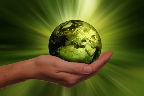 Eine Hand hält eine grüne Erde vor einem hellgrünen Hintergrund.