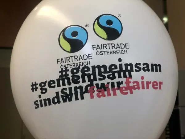 Ein weißer Ballon zeigt das Fairtrade-Logo und den Text '#gemeinsamsindwirfaire', was auf Deutsch 'Zusammen sind wir fairer' bedeutet.