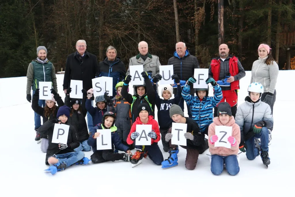 Eine Gruppe von Menschen, darunter Erwachsene und Kinder, posiert für ein Foto auf einem verschneiten Feld und hält Buchstaben hoch, die ein Wort bilden.