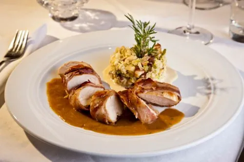 Ein weißer Teller mit einem Gericht aus baconumwickeltem Hähnchen und Sauce, garniert mit einem Rosmarinzweig.