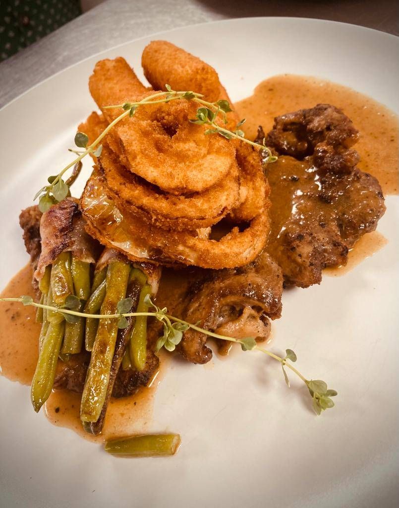 Ein Teller mit knusprigem Zwiebelring, Steak und grünen Bohnen, übergossen mit Sauce und Kräutern.