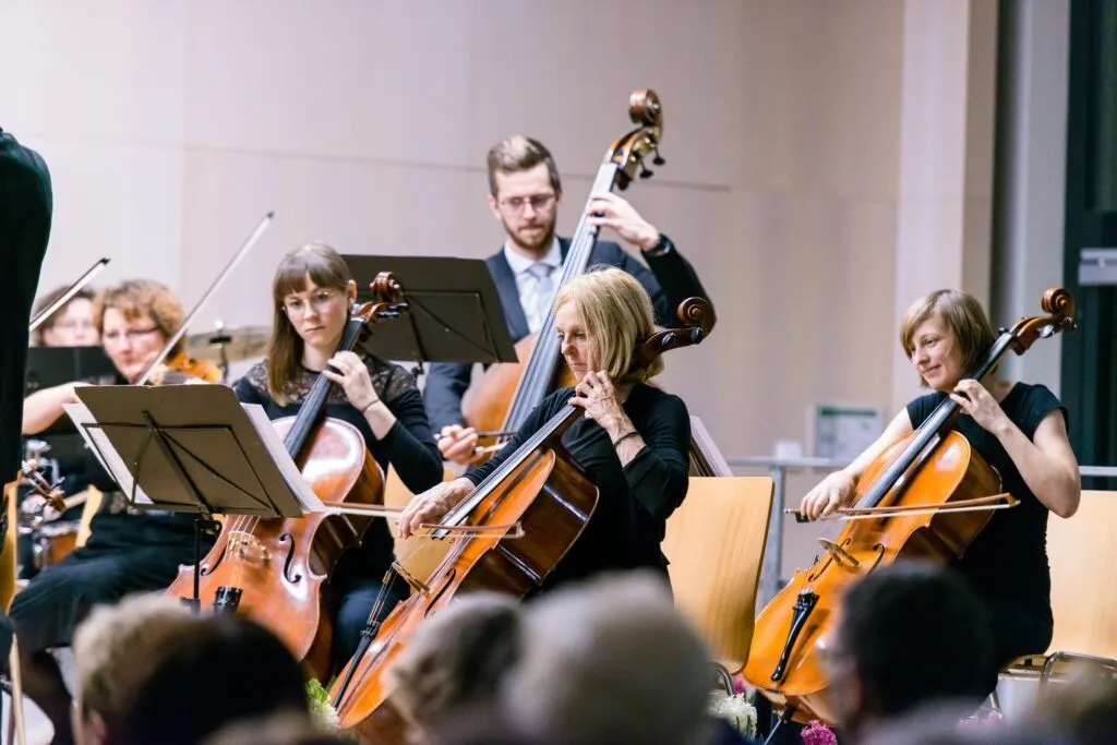 Eine Gruppe von Musikern spielt Cellos auf der Bühne vor einem Publikum. Die Musiker tragen schwarze Langarmshirts.