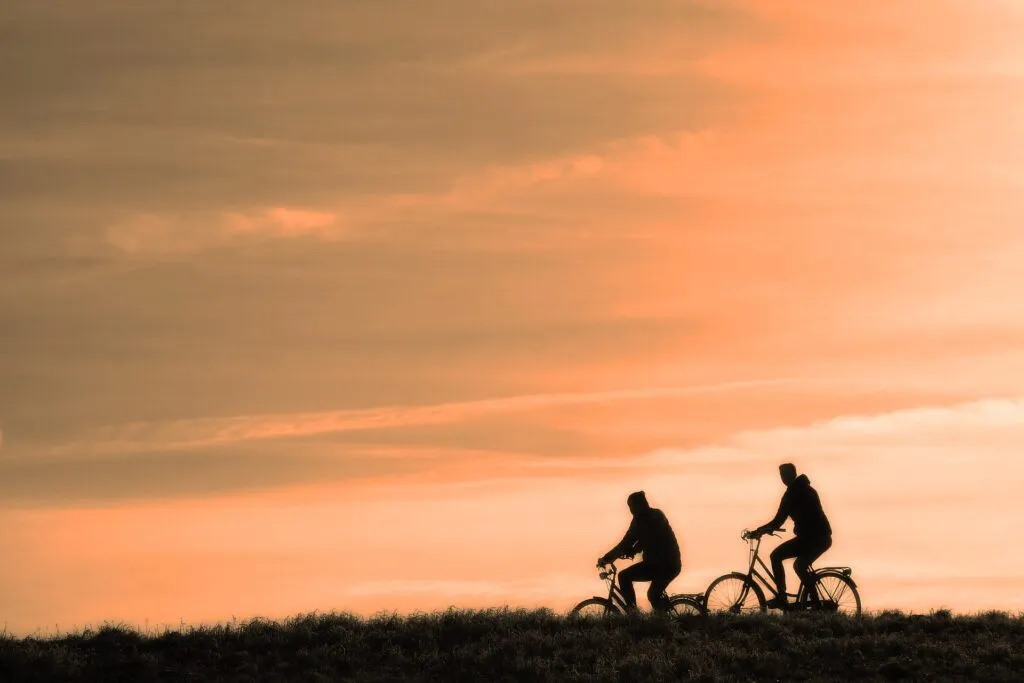 Zwei Radfahrer fahren gegen den Hintergrund eines leuchtenden Sonnenuntergangs auf Fahrrädern, silhouettiert gegen den warmen Himmel.