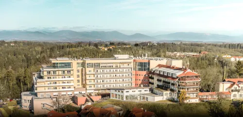 Eine Luftaufnahme eines Gebäudekomplexes mit mehreren Gebäuden, umgeben von Bäumen und Bergen in der Ferne. Die Gebäude haben viele Fenster und sind in verschiedenen Farben gestrichen.