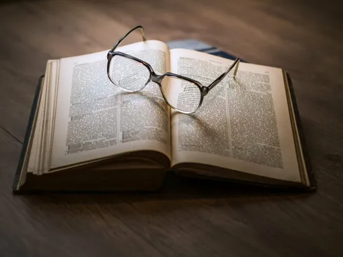 Ein offenes Buch mit einer Brille darauf. Das Buch liegt auf einer Holzoberfläche.