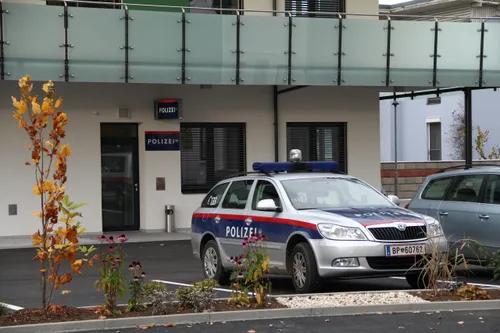 Ein Polizeiauto mit der Nummer 133 ist vor einem Polizeigebäude geparkt. Das Gebäude hat einen Balkon und Schilder mit der Aufschrift Polizei.