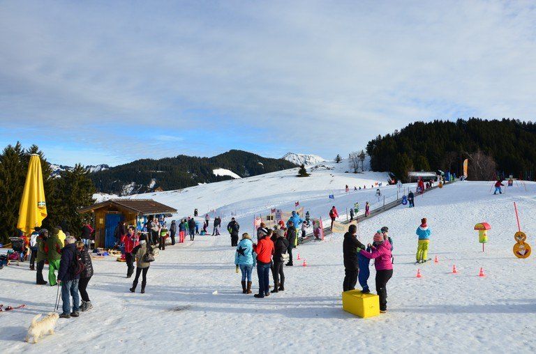 Viele Menschen auf einem verschneiten Berg mit einem gelben Regenschirm, andere sind beim Skifahren und einige stehen in der Nähe von Verkehrskegeln.