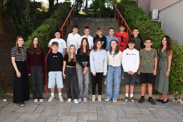 Eine Gruppe von Schülern und zwei Lehrern posiert für ein Foto draußen in der Nähe von Treppen.