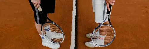 Die Beine eines Tennisspielers sind in weißen Schuhen, Socken und einem Schläger zu sehen. Der Hintergrund ist ein Tennisplatz.