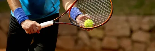 Ein Tennisspieler hält einen gelben Tennisball in der Hand und bereitet sich auf den Aufschlag vor. Er trägt eine blaue Armband und ein blaues Shirt.