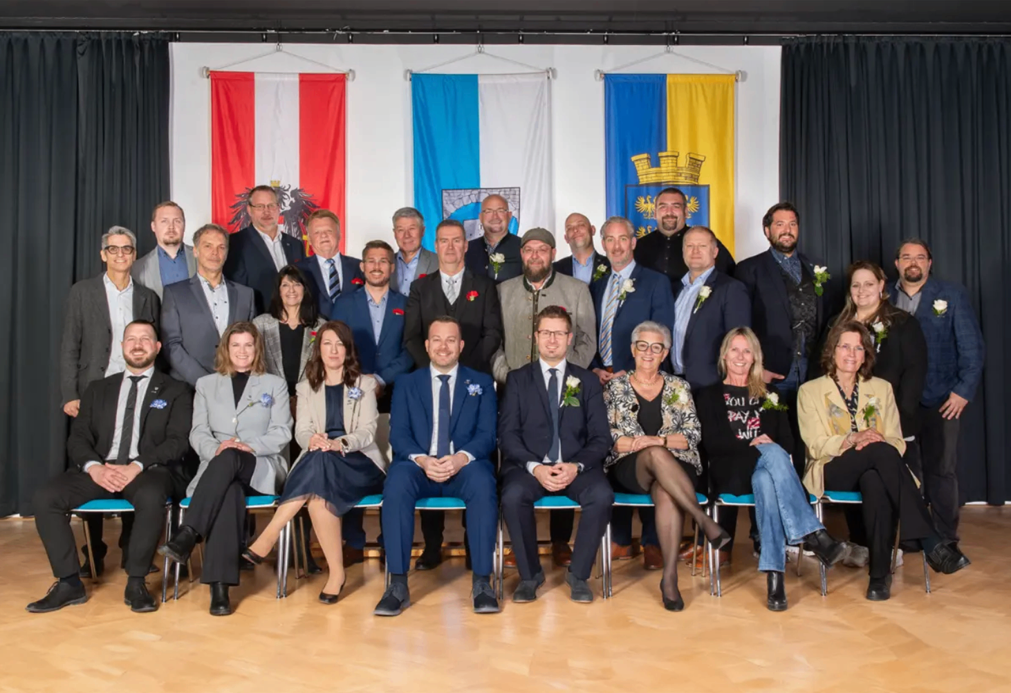 Eine Gruppe von Menschen, Männern und Frauen, posiert für ein Foto vor Flaggen und Bannern. Sie tragen alle formelle Kleidung.