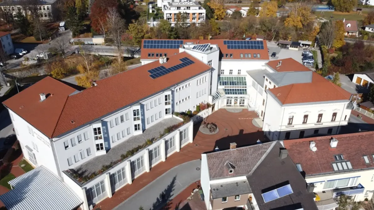 Ein Luftbild eines modernen Gebäudekomplexes mit Solarpanelen auf den Dächern, umgeben von Bäumen und einer Einfahrt.