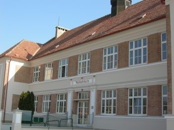 Ein großes Gebäude mit einem roten Dach und vielen Fenstern. Das Gebäude hat ein Schild über dem Eingang, das 'Rathaus' steht.