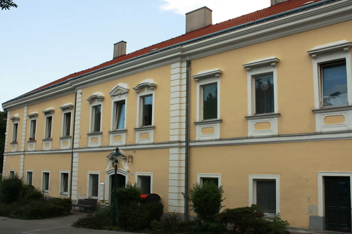 Ein gelbes Gebäude mit einem roten Dach hat mehrere Fenster und eine Laterne davor. Es scheint sich um ein Wohnhaus zu handeln.