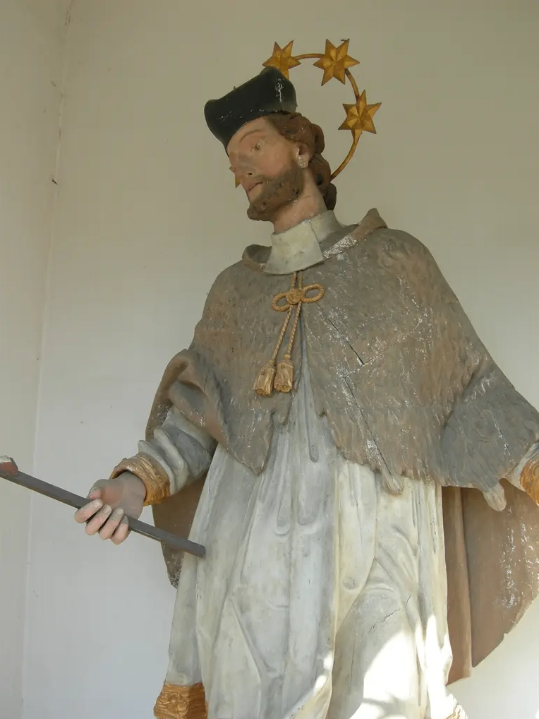 Eine Statue eines bärtigen Mannes mit Hut, der einen Stab mit einem Stern darauf hält, steht an einer Wand.