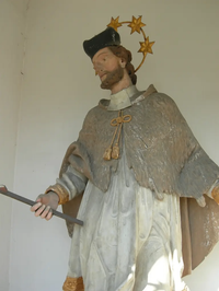 Eine Statue eines bärtigen Mannes mit Hut, der einen Stab mit einem Stern darauf hält, steht an einer Wand.